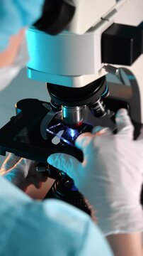 Laboratory technician examining sample under microscope and replacing slide, scientific research process in medical laboratory environment.