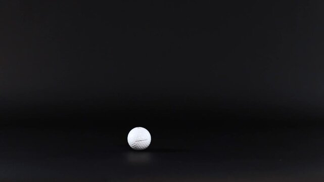 Golf ball rolling slowly across black background in studio lighting cinematic motion footage.