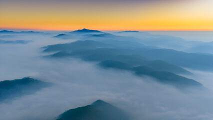 Fototapeta premium A breathtaking sunrise over layers of misty mountains, where the glowing sun forms a radiant starburst in a golden sky. Soft fog blankets the valleys, creating depth and a dreamy