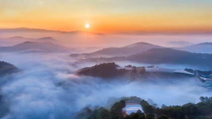 Fototapeta premium A breathtaking sunrise over a sea of clouds in the highlands, where soft layers of mist drift between rolling hills. The warm glow of the rising sun paints the sky in gentle orange and pink tones