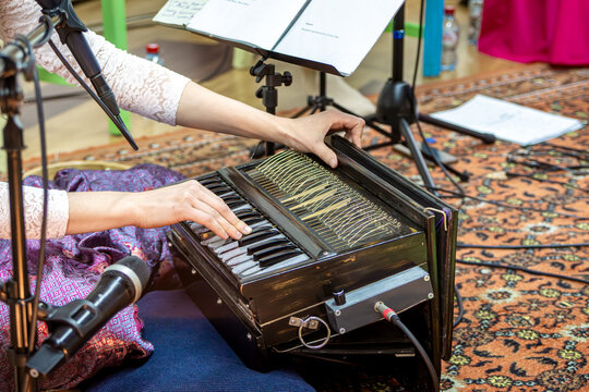 Person plays wooden harmonium with shiny keys at cozy kirtan night while singing sacred mantras into mic