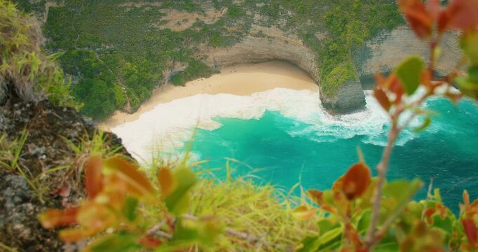 Foamy ocean waves roll onto sandy beach below steep tropical cliffs in Indonesia
