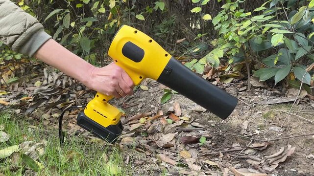 Close-up shot of a gardener's hand holding a compact wireless cordless electric blower