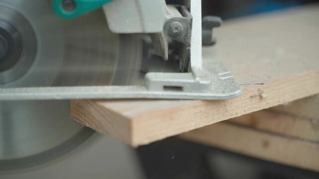 Cutting corner of wooden board with handheld circular saw close-up