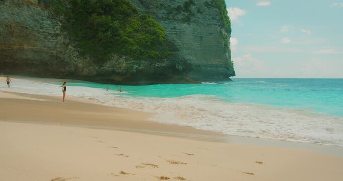 Distant woman enjoying vacations on sandy shore with white foam ocean waves