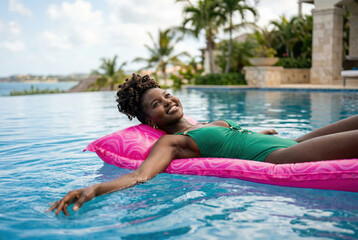 Naklejka premium Beautiful young woman relaxing on a bright pink float in a luxurious swimming pool