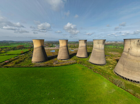 Aerial view of the five Willington Decommissioned Power Station Towers standing in a row surrounded by green fields under a blue sky in Willington, England, United Kingdom.