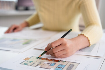 Fototapeta premium Creative female designer works on building design draws sketches floor plan surrounded by samples material and stationery