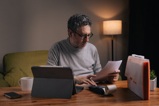 Mature man calculating household expenses and reviewing bills at home