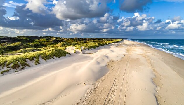 Aerial view of a sandy beach, dunes and ocean under a cloudy sky