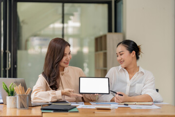 Obraz premium Two Asian businesswomen holding digital tablet with blank white screen for mockup in office.
