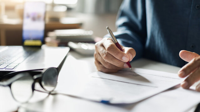 close-up shot, businessman work on desk at home with documents checking business contract, working and meeting online via laptop and mobile phone