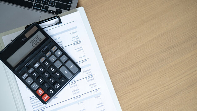 Calculator on financial statement with laptop on wooden desk, business accounting and budget planning concept with office workspace and wide copy space.