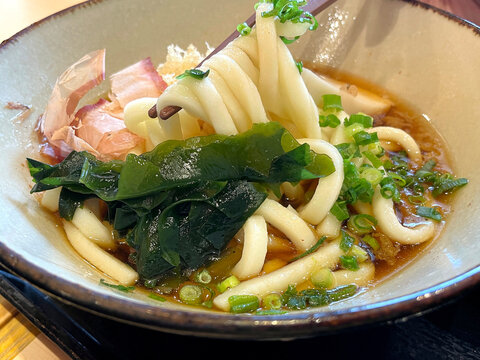 冷たいぶっかけうどん ─ 箸でうどんを持ち上げたアップ・わかめ