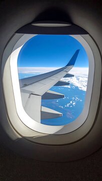 Airplane wing visible from an oval window against a brilliant blue sky