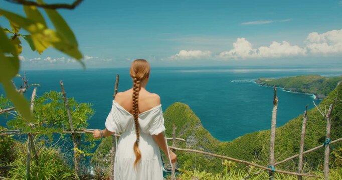 Woman traveler walking at scenic viewpoint and overlooking the iconic T Rex cliff and ocean in Bali Nusa Penida Indonesia
