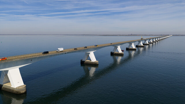Aerial view of the Zeeland Bridge with cars and trucks crossing the Oosterschelde estuary under a clear blue sky in Zierikzee, Zeeland, Netherlands.