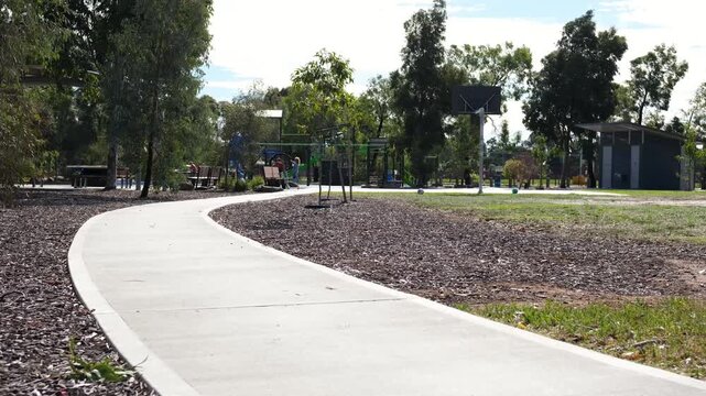 Winding concrete pathway through suburban park, basketball hoop, playground and eucalyptus trees in the distance, Melbourne Australia.&nbsp;Community recreational infrastructure and outdoor public space