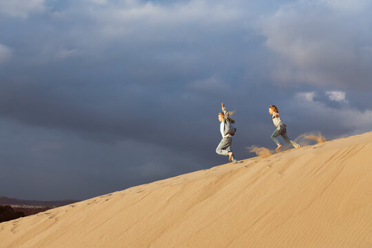 Happy kids run, jump and having fun in sand dunes at Patara Beach, Turkey. Active travel lifestyle, sunny coastal landscape and freedom of movement during vacation in popular tourism destination