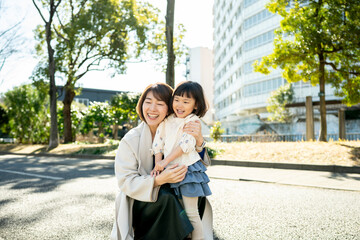 Fototapeta premium Japanese mother hugging her toddler daughter in the park with soft sunlight