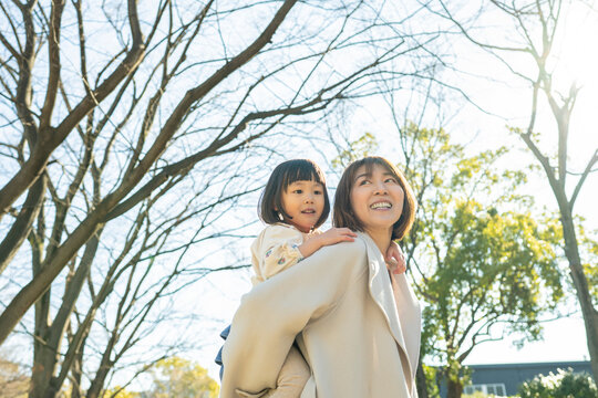 Smiling Japanese Mother and Toddler Daughter Looking Up at the Trees in a Sunny Park