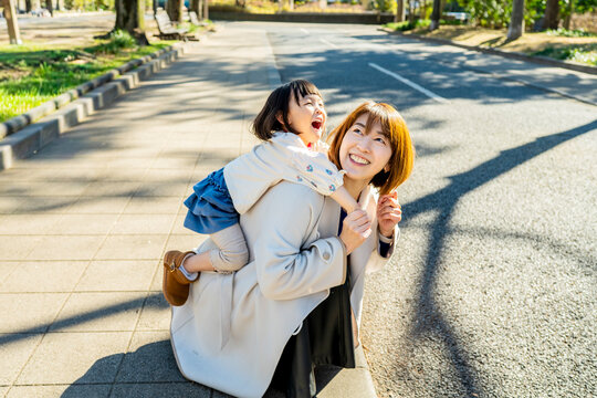 Joyful Japanese Mother and Little Daughter Laughing Together Outdoors in Sunlight