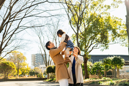 Joyful toddler girl being lifted high in the air by her parents in a winter park, happy family smiling together