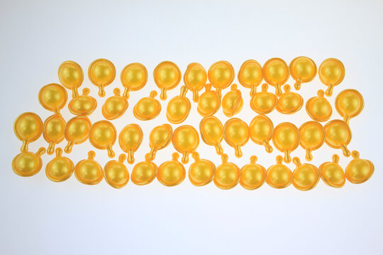 Golden hair serum capsules arranged neatly on a plain white background. Bright, translucent yellow uniform color suggests high quality, products. For self care, hair nutrition, vitamin E hair serum.