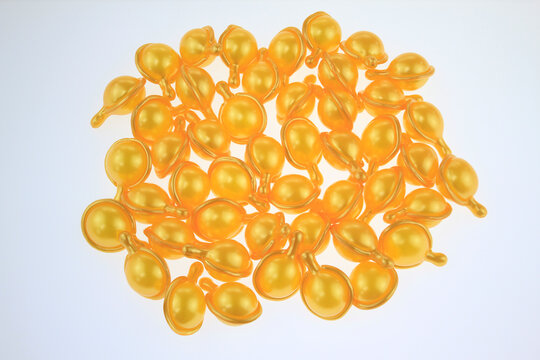 Golden gel  hair serum capsules gleam softly isolated on white background. Each capsule reflects light with smooth, rounded contours.  For hair care routine, hair nutrition, damaged hair repair, serum