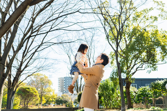 Happy Japanese father lifting his young daughter high in a sunny winter park, family joy