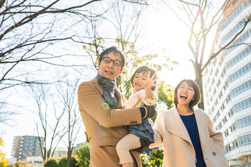 Fototapeta premium Toddler girl being held by her father and waving at the camera in a winter park, family portrait