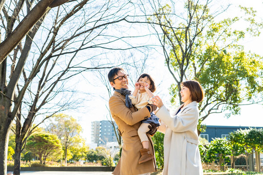 Cute toddler girl winking while being held by her father, parents laughing together in a winter park