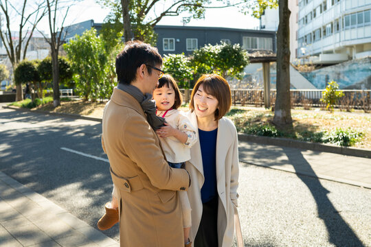Happy Japanese family walking together on a paved path in an urban park on a sunny winter day, full-length shot