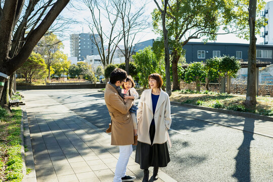 Happy Japanese family walking together on a paved path in an urban park on a sunny winter day, full-length shot