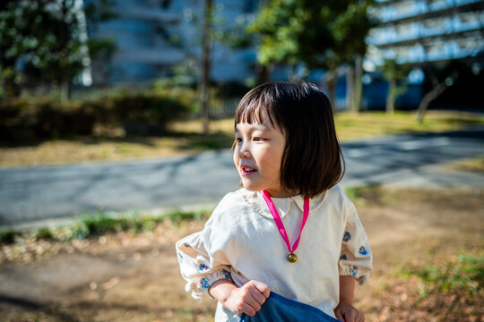 Portrait of a cute Japanese toddler girl smiling and looking away in a sunny winter park