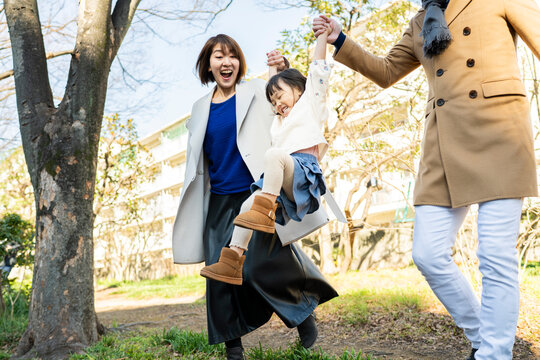 Joyful Japanese parents lifting their little daughter high towards the sunlight in a bright winter park, family happiness
Keywords: