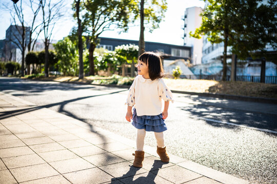 Cute Japanese little girl standing and smiling in a sunny park landscape
