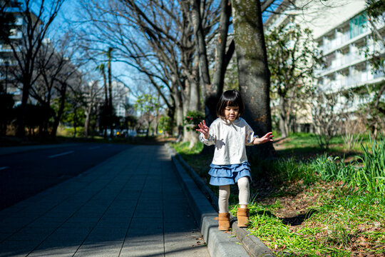 Cute Japanese little girl standing and smiling in a sunny park landscape