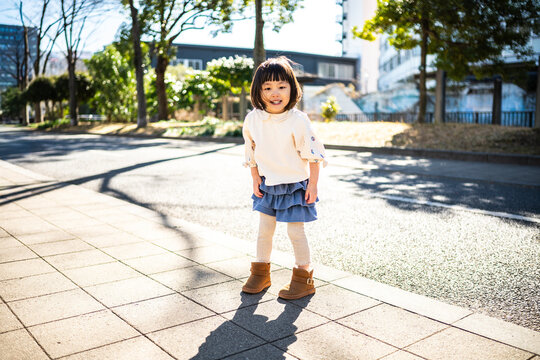 Cute Japanese little girl standing and smiling in a sunny park landscape