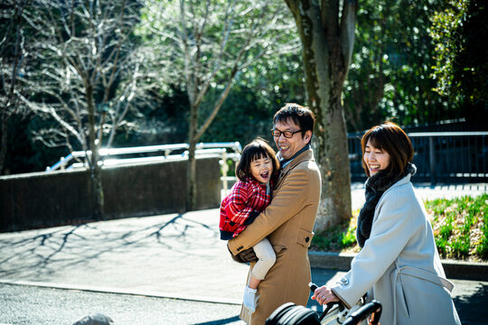 Happy Japanese parents walking together in a park while father carrying little daughter