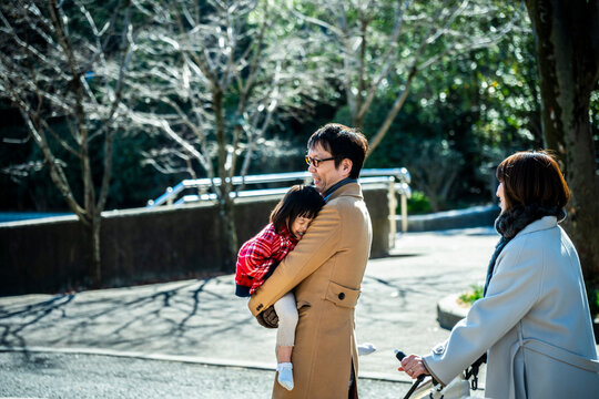 Tired Japanese little girl sleeping on her father's shoulder during a family walk