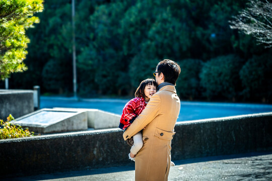 Loving Japanese father holding his little daughter in his arms at a sunny park