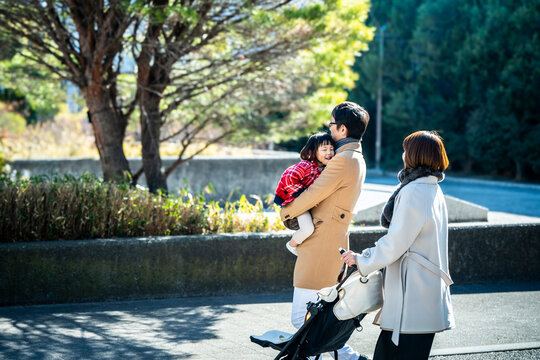 Happy Japanese parents walking together in a park while father carrying little daughter