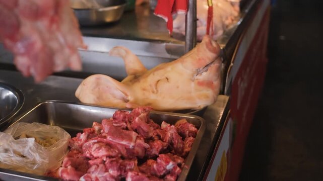 Market butcher counter displaying pork cuts and pig head with raw meat pieces arranged for sale. Traditional meat market concept