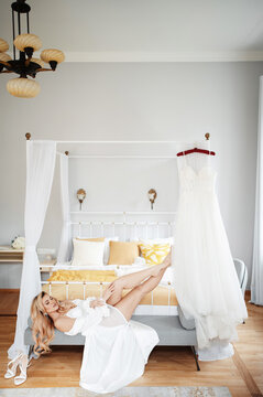 Bride in white lingerie relaxing on a bench near her wedding dress