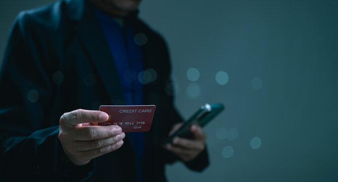 Businessman holding credit card plus smartphone performs secure digital transaction online. Professional male wearing suit manages personal finance, electronic banking, mobile shopping, internet