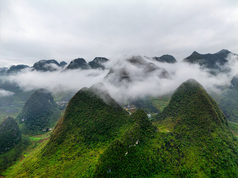 Aerial view of the Ha Giang Loop featuring lush green karst mountains partially covered by thick white mist under a cloudy sky in Vietnam.