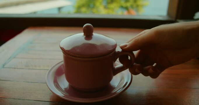 Hand lifts lid of pink ceramic coffee cup on wooden table in Bali Nusa Penida Indonesia