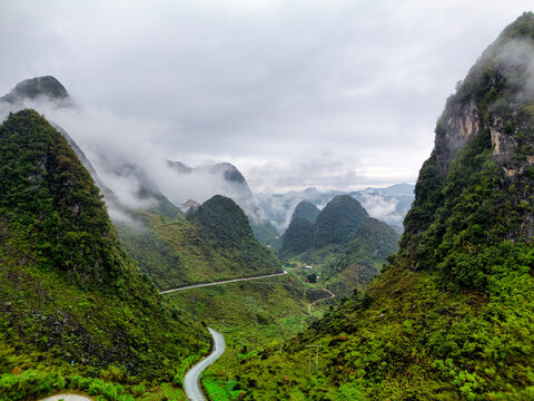 Aerial view of the winding mountain road of the Ha Giang Loop passing through lush green karst peaks and misty valleys in Vietnam.