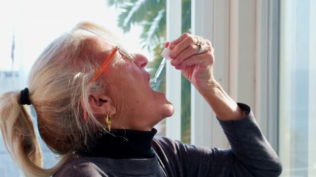 Close-up of a mature senior woman taking liquid vitamins or herbal supplement with a dropper. Concept of healthy aging, daily wellness routine, and natural medicine for longevity and self-care